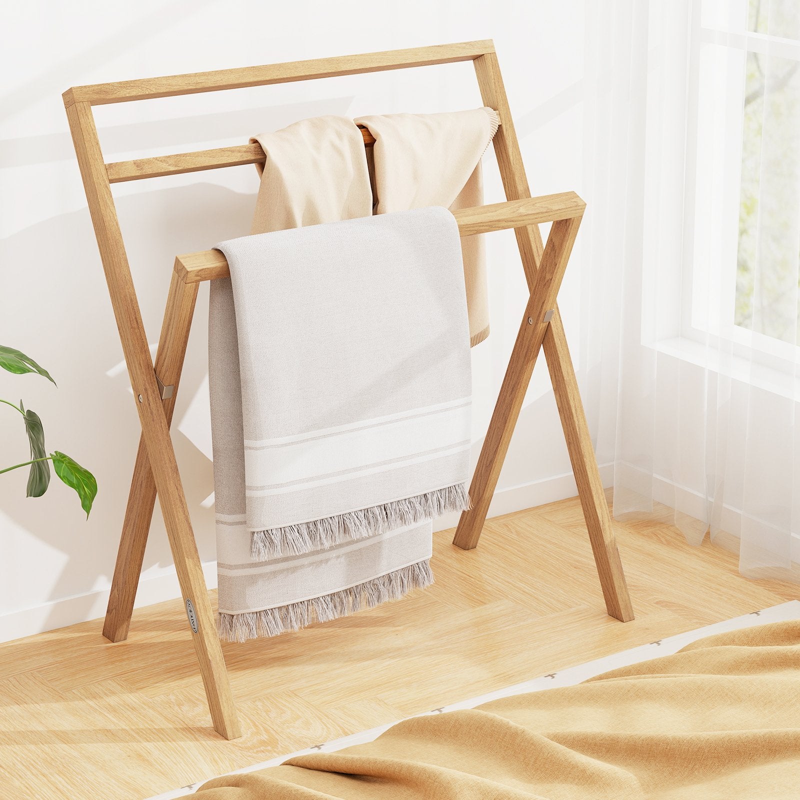 Freestanding foldable teak wood towel rack with three crossbars for hanging towels in a bathroom setting.